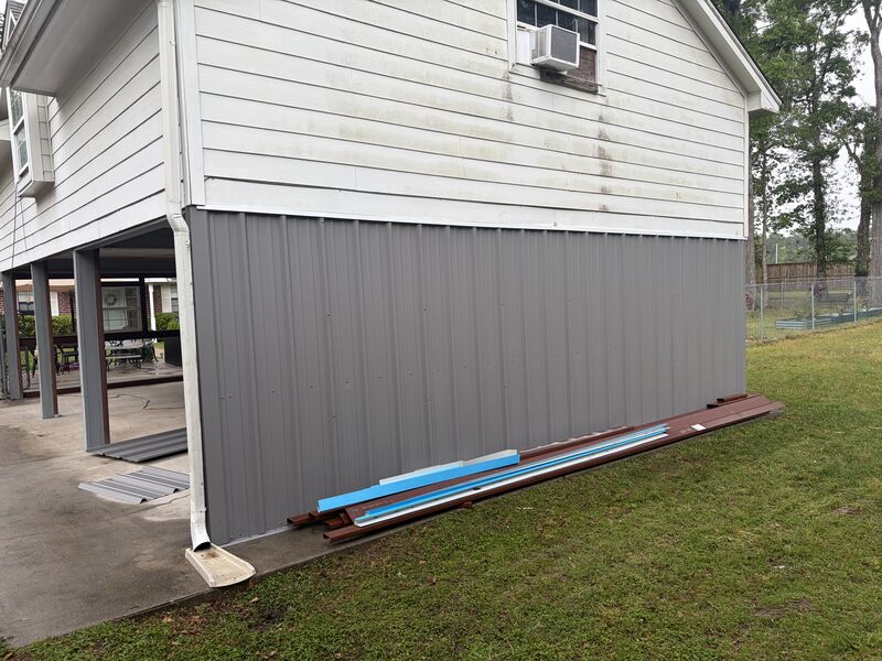 Grey metal siding going up on the lower level with panels stacked on site