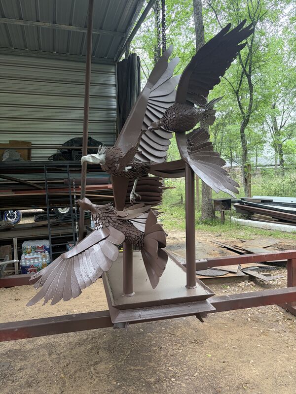 Mounted eagle sculptures seen against the shop yard and steel stock racks